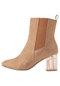 Botín estilo ballet en color beige con parte superior adornada con rhinestones, paneles laterales elásticos y tacón bloque transparente. Diseño de puntera afilada.