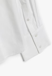 Chemise en coton blanche avec un col classique, des boutons de fermeture et des manches retroussées avec de subtils détails de couture. Texture lisse, coupe droite.