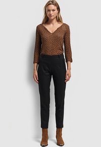 Haut à manches longues imprimé léopard marron avec un col en V, associé à un pantalon noir à rayures taille haute et des bottines en daim marron.