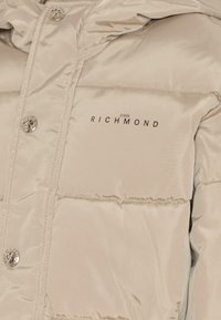 Giacca imbottita beige con finitura lucida, caratterizzata da bottoni argentati, pannelli cuciti e il nome del marchio "JOHN RICHMOND" in nero.