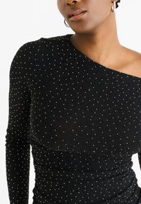 Black one-shoulder top made of ribbed fabric, adorned with silver dots and featuring a fitted silhouette with gathered detailing.