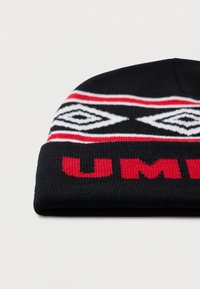 Čierna pletená čiapka s ohnutým okrajom, na ktorej sú červené písmená a biele geometrické diamantové vzory orámované červenými pruhmi.