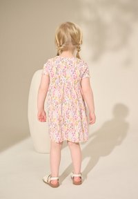 Robe en coton à fleurs roses avec manches courtes, taille froncée et ourlet festonné. Portée avec des sandales blanches. Texture douce et légère.