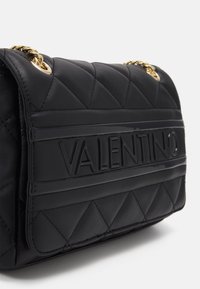 Borsa a tracolla in pelle trapuntata nera con logo "VALENTINO" prominente, hardware in catena dorata e dettagli testurizzati sulla patta.