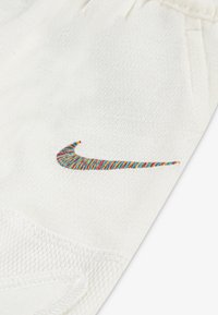 Hvide stofshorts med en farverig broderet Nike swoosh-logo, med struktureret syning og mesh-detaljer ved lommeområdet.