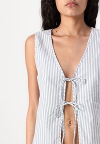 Haut sans manches rayé en tissu léger, avec un décolleté en V profond et un nœud central, comportant une découpe en trou de clé et des accents en ruban.