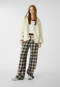 Cremfarbener Fleece-Reißverschlussjacke, weißes geripptes Oberteil, braune karierte Schlaghose und silberne Sneaker. Strukturiertes Gewebe mit lockerem Schnitt.