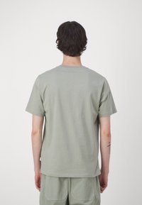 Camiseta de manga corta verde claro hecha de algodón, con un escote redondo y una textura lisa y uniforme. Sin logotipos ni patrones visibles.