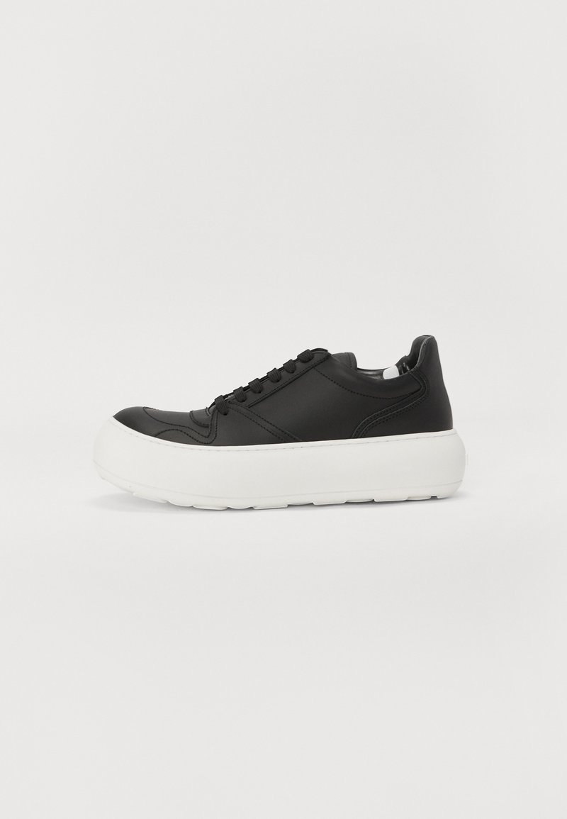 Zwarte leren sneaker met een dikke witte rubberen zool, ronde neus en platte zwarte veters. Gladde textuur met gestikte accenten.