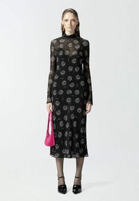 Crna haljina dugih rukava s tijesnim siluetom, prozirna tkanina, spiralni srebrni uzorak, uparena s ružičastom torbicom i crnim lakiranim cipelama.