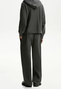 Vaffelmönstrad, mörkgrå hoodie med huva och muddar vid ärmarna, ihop med matchande löst sittande byxor som har sidofickor och en avsmalnande design.