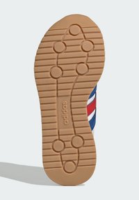 Rubber shoe sole with a herringbone pattern and circular grips. Textured beige material with ‘adidas’ branding near the heel.