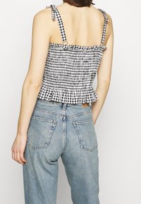 Haut péplum en gingham noir et blanc avec bretelles à nouer ajustables, corsage froncé et ourlet à volants ; accompagné d'un jean taille haute bleu clair.