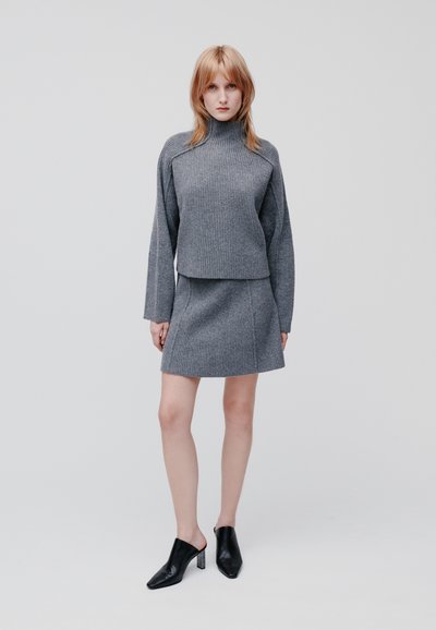 Grauer gerippter Pullover mit hohem Kragen und langen Ärmeln, kombiniert mit einem grauen gerippten Minirock. Schwarze Absatzmules runden das Outfit ab.