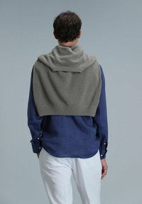 Grijze gebreide trui over een marineblauwe shirt, met ribbels aan de mouwen en een textuurafwerking, tegen een lichtgrijze achtergrond.