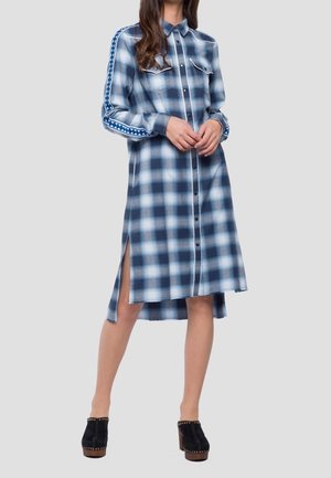 Niebiesko-biała sukienka w kratę na guziki z długimi rękawami, wzorzysty pasek na ramionach, boczne rozcięcia, noszona z czarnymi drewniakami na platformie.