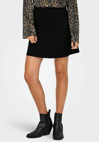 Kobieta w czarnej spódnicy w kształcie litery A, długim rękawie w wzór lamparcze, czarnych botkach za kostkę oraz dwóch pierścionkach na palcach.