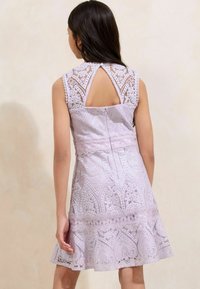Rochie din dantelă lavandă cu motive florale intricate, design fără mâneci și detaliu de tip cheie la spate. Prezintă un tiv evazat și o țesătură texturată.