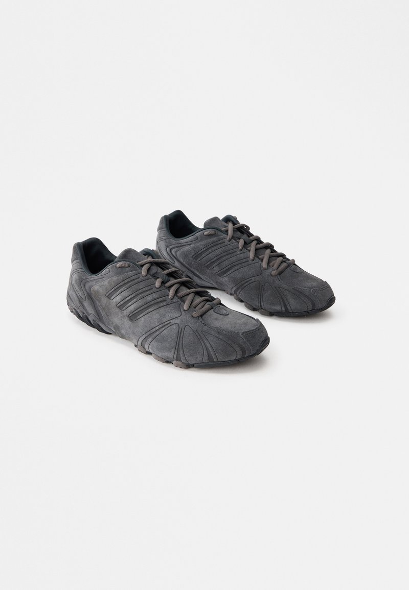 Μαύρα σουέτ αθλητικά παπούτσια με γραπτή επιφάνεια, καμπύλο σχέδιο και ελαστικές σόλες. Διαθέτουν κορδόνια και οριζόντιες ρίγες στα πλάγια.