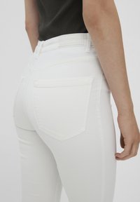 I jeans bianchi presentano un design aderente con una texture liscia. Sono visibili due tasche posteriori di forma rettangolare con dettagli di cucitura bianca.