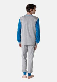 Set di pigiama grigio in cotone composto da una maglietta a maniche lunghe con maniche e polsini blu, pantaloni grigi abbinati, e una vestibilità rilassata. Tessuto testurizzato.