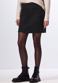 Mini gonna in misto lana di color grigio scuro, con due tasche frontali, vita attillata e una consistenza morbida. Abbinata a stivaletti neri con lacci.