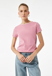 Camiseta corta de manga corta en color rosa con escote redondo y ribetes en contraste. Se lleva con unos vaqueros de denim de color azul claro. Tejido suave, diseño ajustado.
