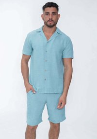 Chemise à manches courtes bleu clair avec boutons et shorts assortis en tissu texturé. Présente un col évasé et des poches avant.