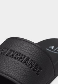 Κοντινό πλάνο του λουριού μαύρου διαβαθμισμένου σαγιοναριού με ανάγλυφη επιγραφή "ARMANI EXCHANGE".