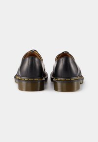 Pantofi din piele neagră cu tocuri rotunde, accente de cusături galbene și textură netedă. Designul prezintă un stil clasic de tip slip-on.