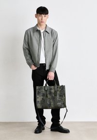 Borsa a spalla con motivo camouflage in tonalità verdi, realizzata in tessuto resistente, dotata di manici doppi, una tracolla rimovibile e un'etichetta.