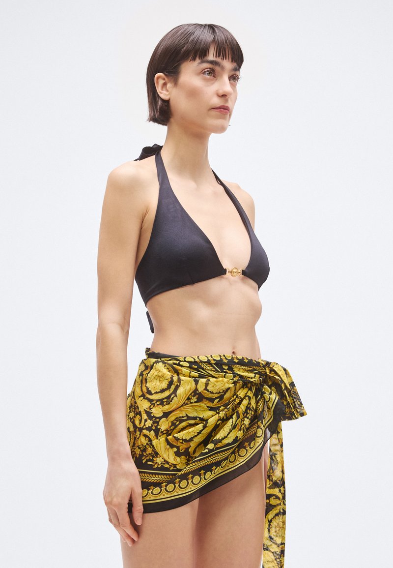 Black bikini top with halter neck and gold hardware; yellow and black patterned wrap skirt tied at the waist. Smooth fabric textures.