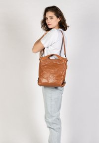 Braune Leder-Schultertasche mit strukturiertem Finish, ausgestattet mit einem Handgriff und verstellbarem Riemen. Die Form ist rechteckig mit abgerundeten Ecken.