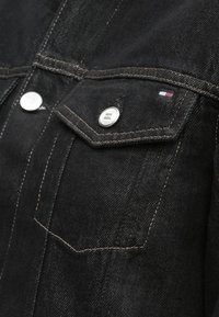 Melna džinsa jaka ar sudraba kniedēm, divām priekšējām kabatām ar atlokiem un kontrastējošu gaiši brūnu šuvi.