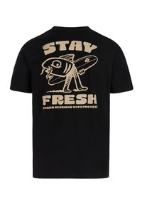 Camiseta de algodón negra con un gran gráfico beige de un pez con una tabla de surf y el texto "STAY FRESH" en la espalda.