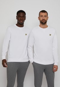 White sweatshirts with crew necks, featuring small yellow butterfly logo on the left chest. Paired with gray sweatpants, relaxed fit.