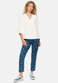 White, V-neck blouse with three-quarter sleeves. Blue jeans featuring a textured, patterned design. Light blue sneakers complete the outfit.