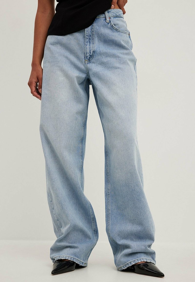 Jean large bleu clair en denim. Présente un design classique à cinq poches et un léger délavage. Porté avec des chaussures noires à bout pointu.