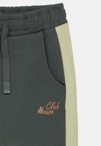 Tmavě zelené tepláky se světle zeleným pruh na boku, elastickým pasem a vyšitým logem "Club House" v hnědé barvě. Měkká textura.