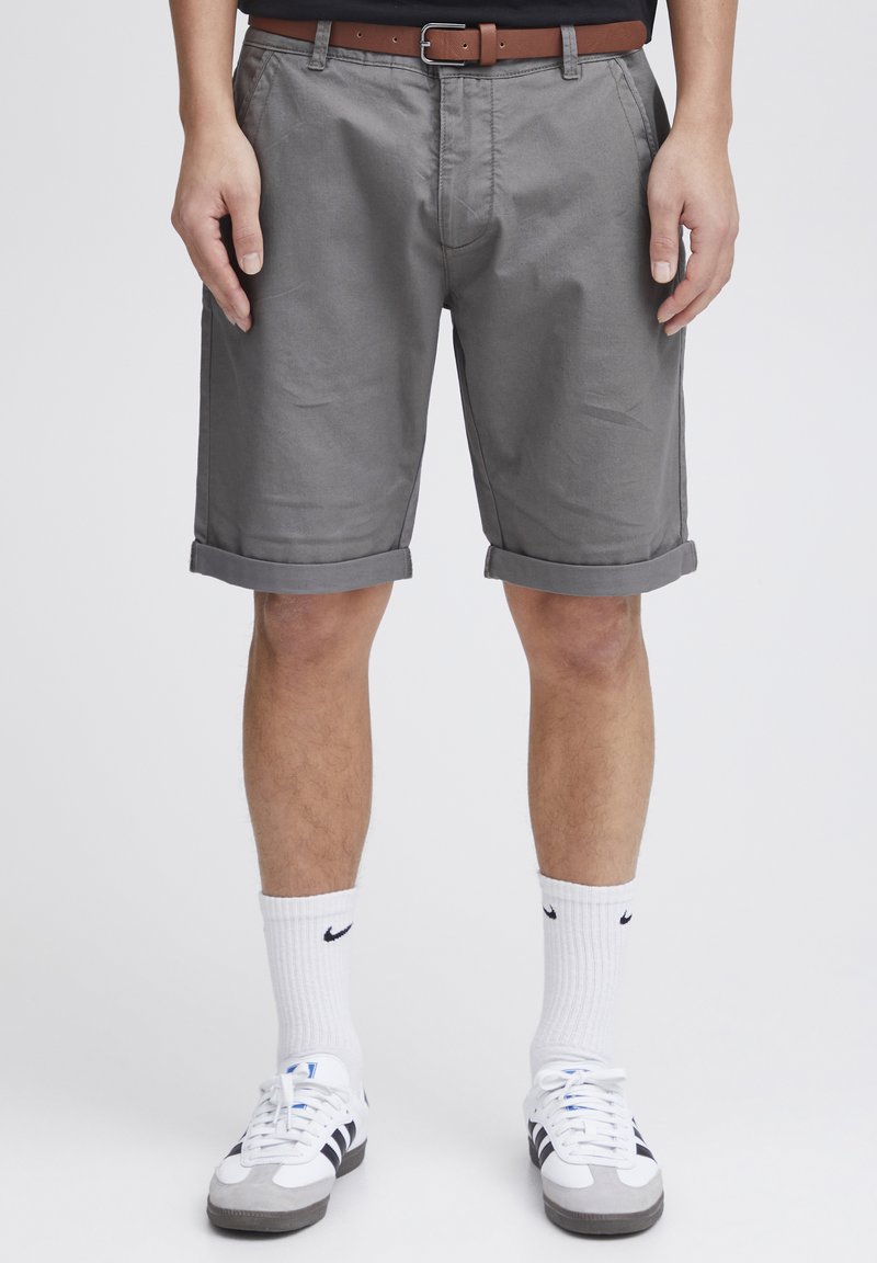 Grå bomullsshorts med rullekanter, et brunt belte og hvite sokker kombinert med grå og svarte joggesko. En enkel, rett passform.