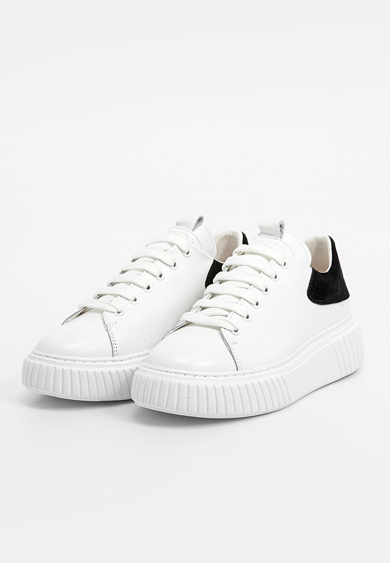 Weiße Leder-Sneaker mit einem strukturierten schwarzen Wildleder-Heel, runder Zehenform und weißer Gummiplattformsohle. Ausgestattet mit weißen Schnürsenkeln und Nähdetails.