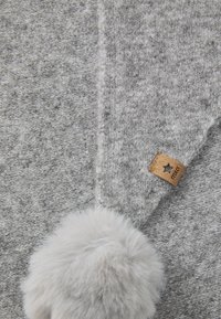 Grått tyg med en mjuk textur, med en fluffig ljusgrå pom-pom och en brun etikett märkt "mixo." Designen är enkel och funktionell.