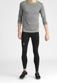 Outfit sportivo da uomo: maglietta grigia a maniche lunghe con cuciture gialle, leggings neri e sneakers nere con dettagli a fantasia.