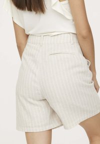 Shorts rayés beiges en tissu léger, avec une poche arrière et une coupe ajustée légèrement évasée.