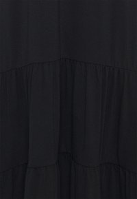 Musta mekko kerroksellisella muotoilulla, jossa on kokoontuneita tekstuureja ja sileää, pehmeää kangasta. Kangas näyttää hienovaraisia vaihteluita valossa.