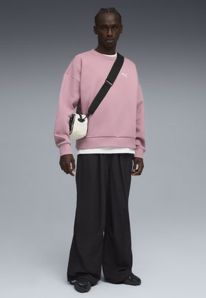 Pink sweatshirt med rund hals, parret med oversized sorte bukser. En lille hvid crossover taske med en sort rem. Sorte sneakers.