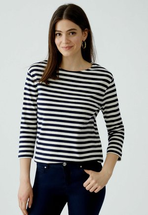 Navy en witte gestreepte katoenen top met lange mouwen en ronde hals. Het model draagt het met donkere jeans, wat een relaxte pasvorm en een soepele textuur laat zien.
