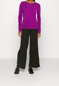 Top de manga larga morado con escote redondo, combinado con pantalones anchos negros. Mocasines negros completan el atuendo. Texturas de tela suaves visibles.