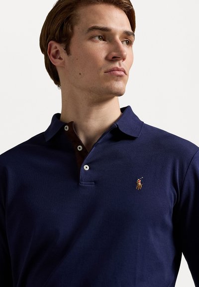 Navy polo shirt with a two-button placket and a brown textured collar. Features a small embroidered logo on the left chest. Smooth fabric texture.