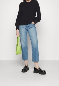 Svart stickad tröja med puffärmar, ljusblå raka jeans, svarta chunky loafers och en klargrön axelväska.